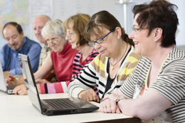 Senioren sitzen im Seminarraum an Laptops